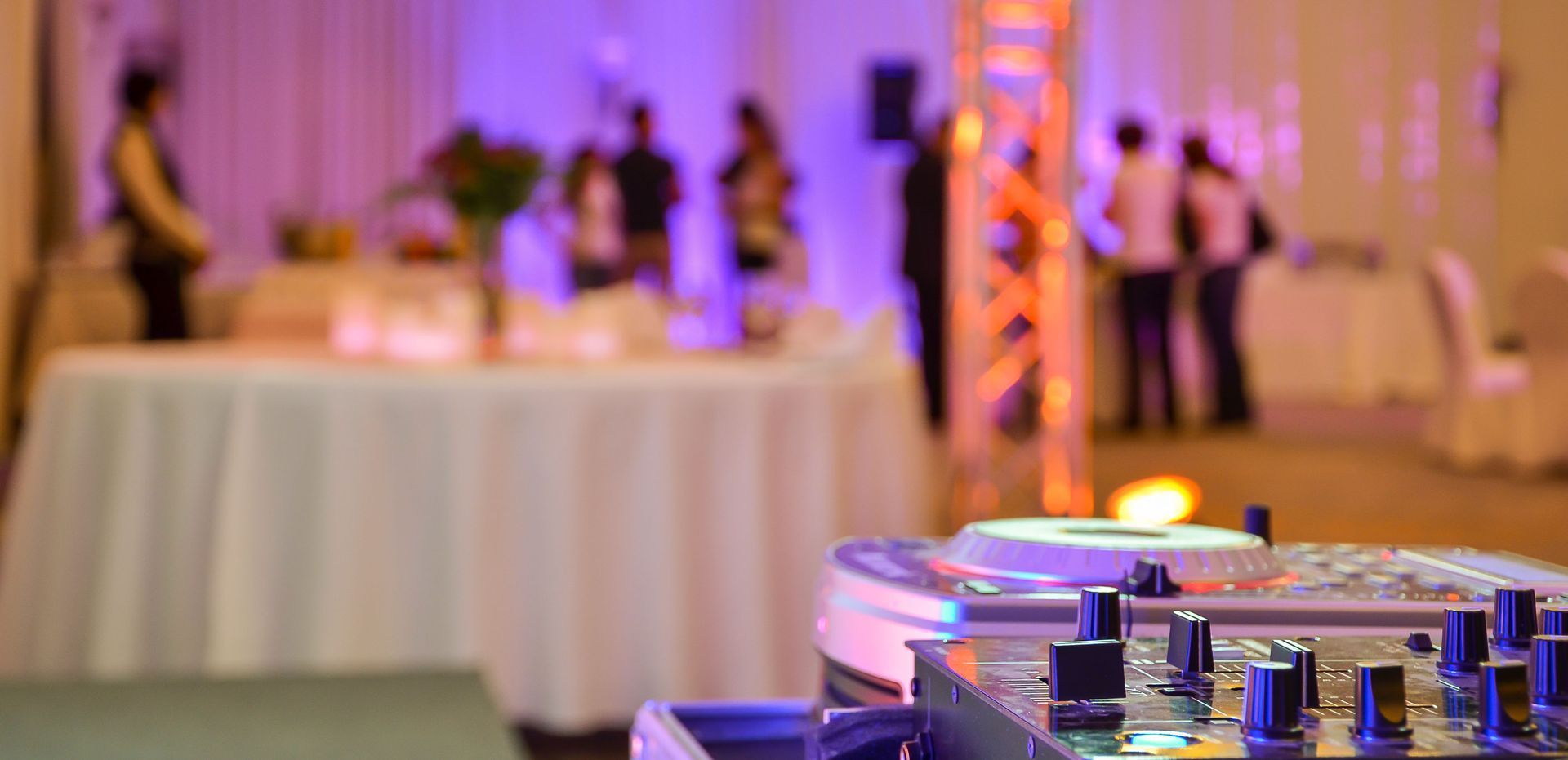 DJ turntable in the foreground with a blurred party crowd and buffet tables in the background