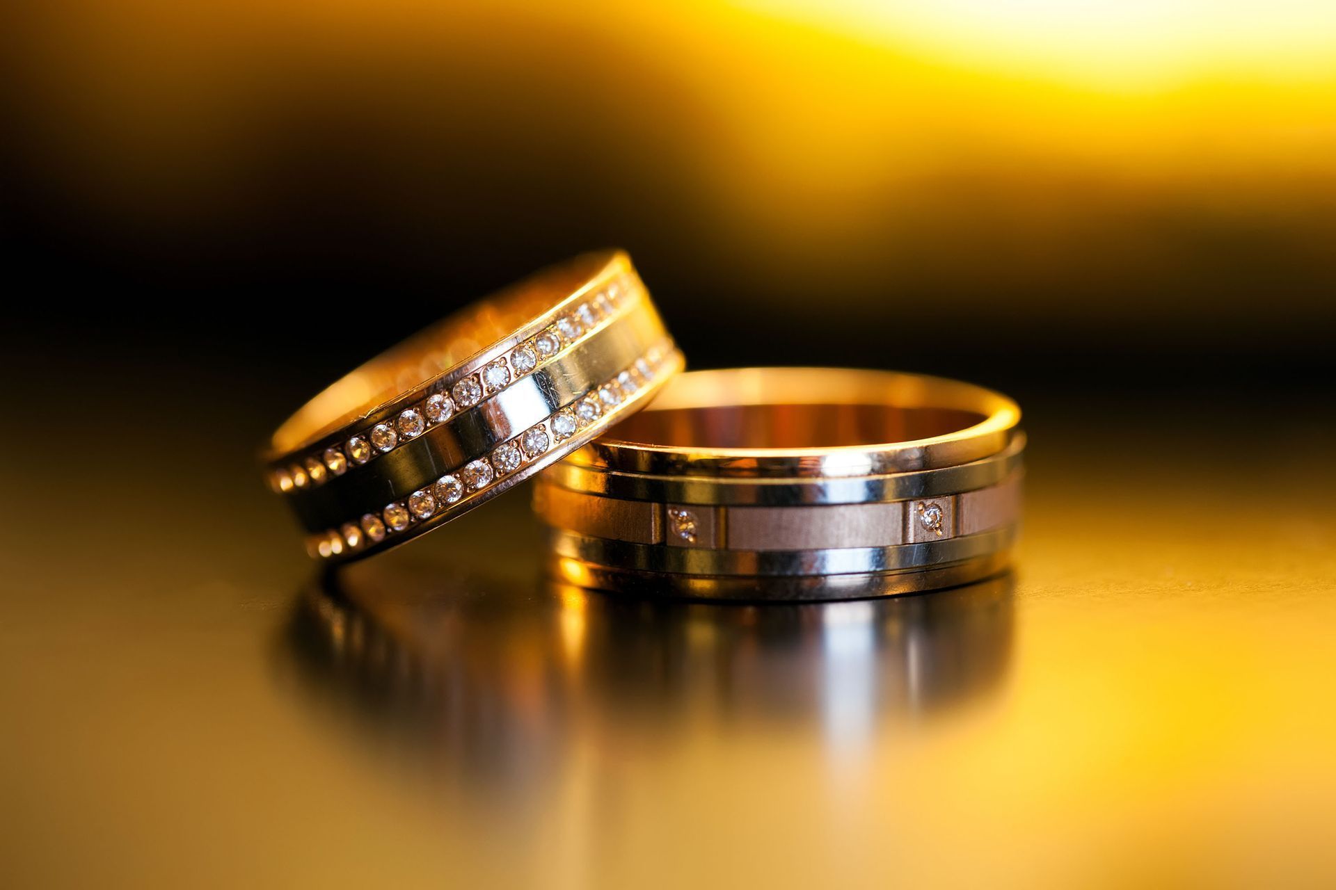 Two gold wedding bands on a reflective surface with warm golden light