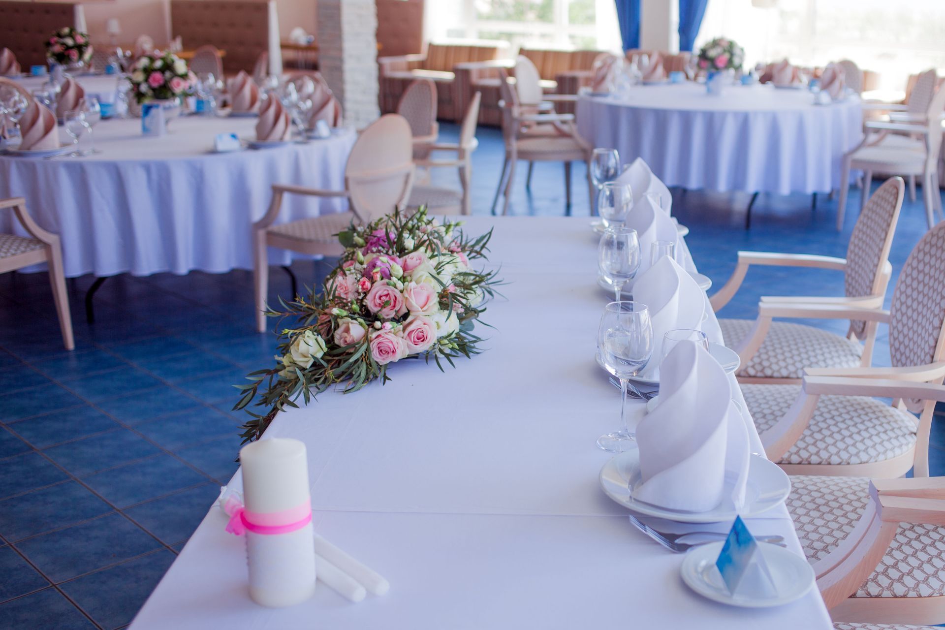 Decorated banquet table with white linens, floral centerpiece, and folded napkins in a bright event hall