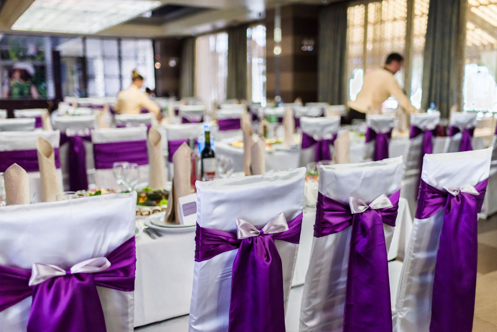Banquet hall with rows of white chairs tied in purple sashes and set tables in the background