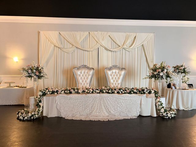 Elegant wedding reception backdrop with cream drapery, floral arrangements, and two ornate chairs behind a decorated table