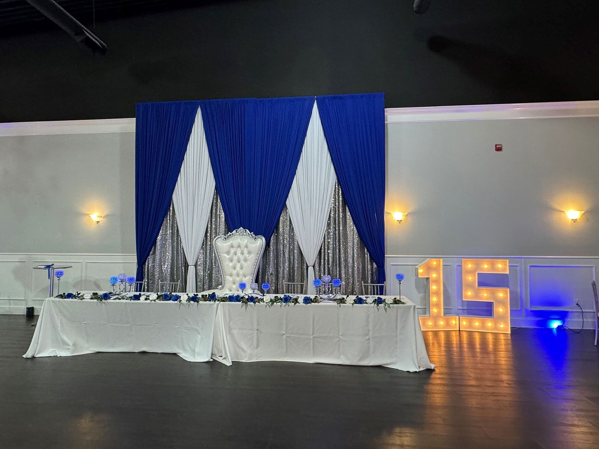 Elegant banquet table with blue and white drapery backdrop and glowing “15” lights in a hall