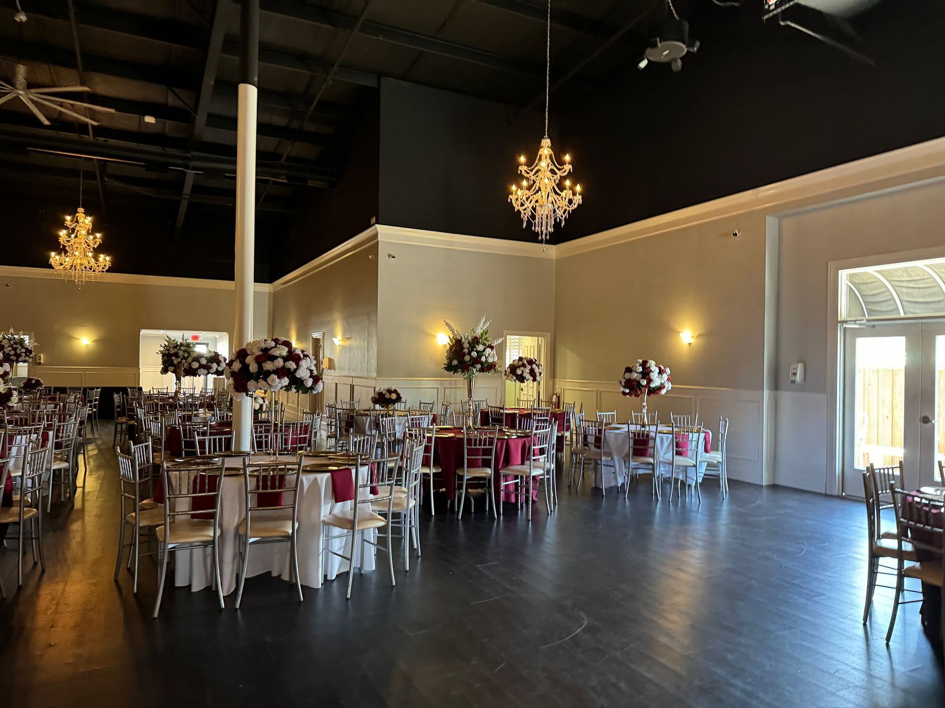 Elegant banquet hall with chandeliers, round tables, white chairs, and dark wood floors
