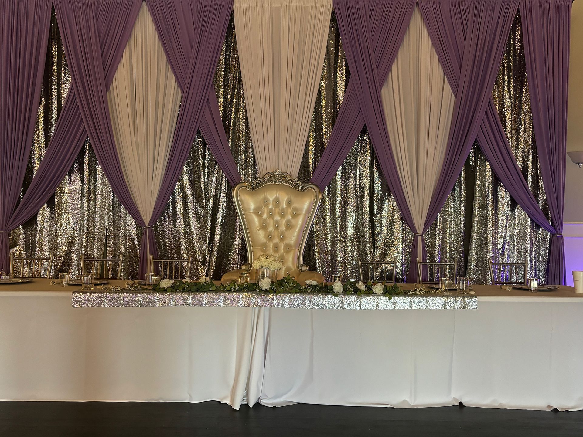 Decorated stage with purple drapes, silver backdrop, and white table/skirted front panel