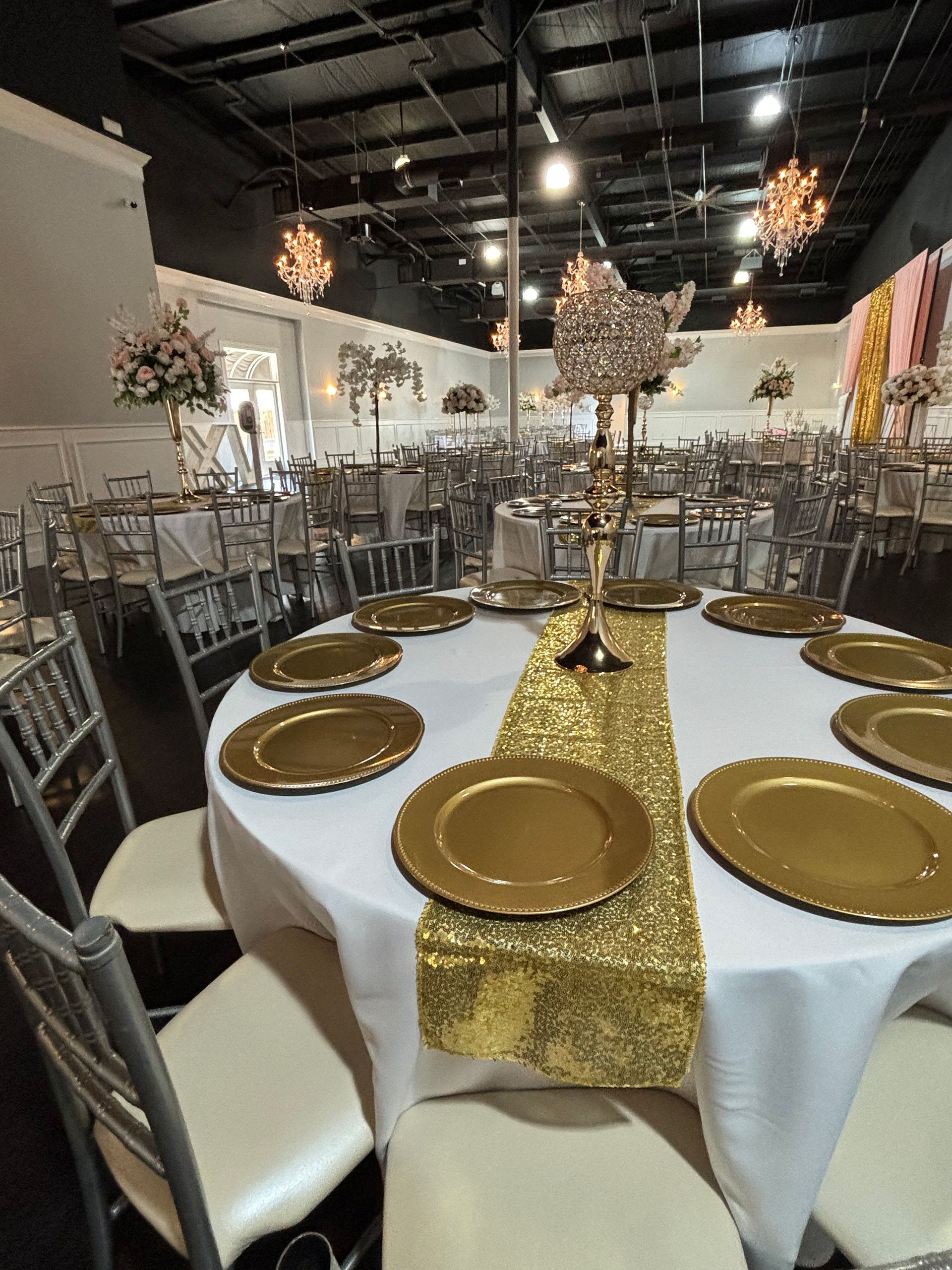 Decorated banquet table with gold plates, white chairs, and a gold sequin runner in an event hall