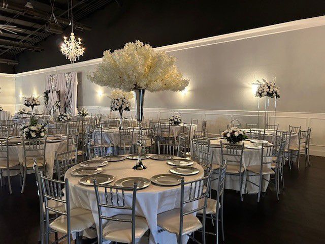 Elegant banquet hall with round tables, silver chairs, and tall white floral centerpieces