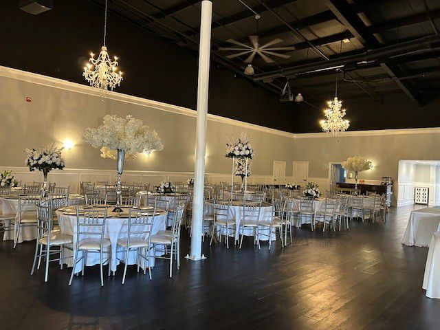 Elegant banquet hall with round tables, white chairs, chandeliers, and dark wood floors