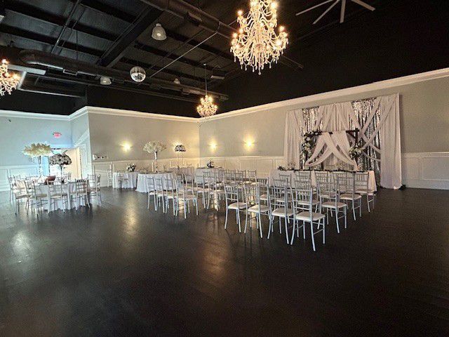 Elegant event hall with chandeliers, black ceiling, white tables and chairs, and a glossy dark floor