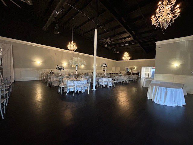 Empty banquet hall with white-clothed tables, chairs, and hanging chandeliers on a dark floor