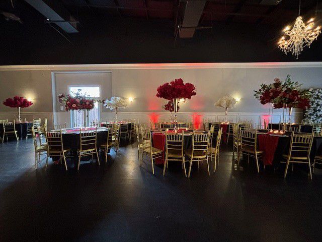 Elegant banquet hall with round tables, gold chairs, red floral centerpieces, and soft ambient lighting