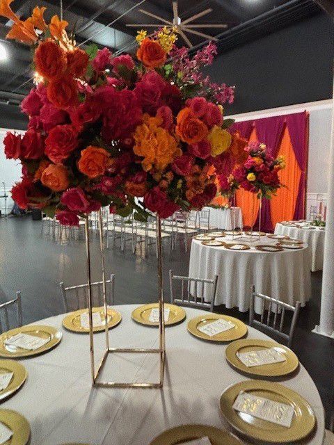 Tall floral centerpiece with red, orange, and pink flowers on a decorated banquet table