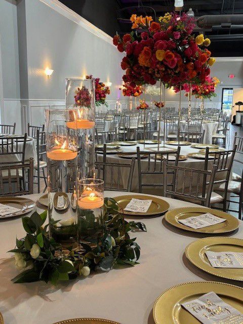 Elegant reception table with gold chargers, candles, and a hanging floral centerpiece in a bright ballroom