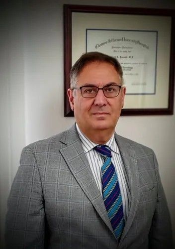 Man in gray suit and striped tie standing indoors beside a framed certificate on the wall