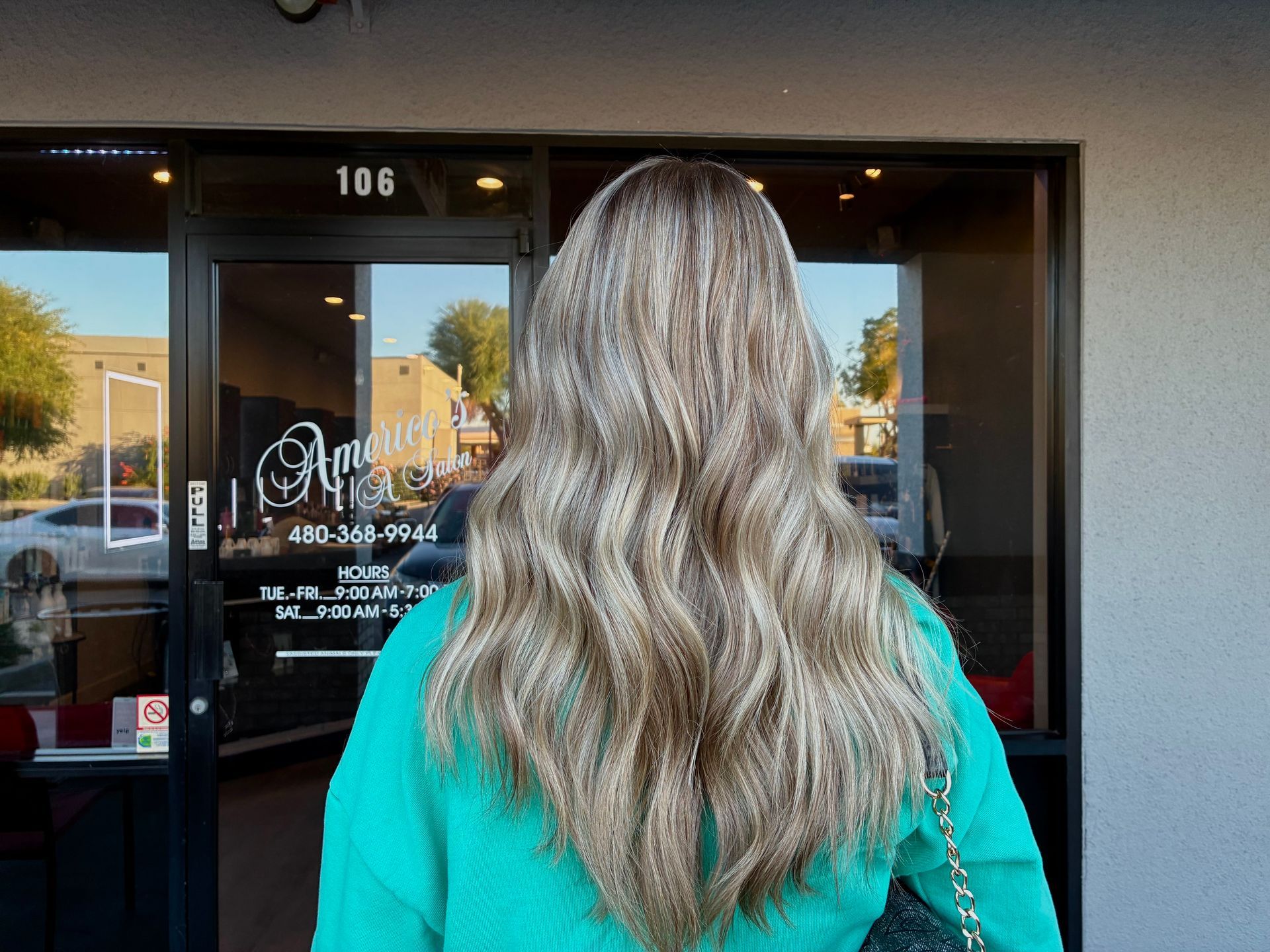 Woman with long, wavy blonde hair enters a shop. She wears a turquoise sweater. Shop has the number 106.