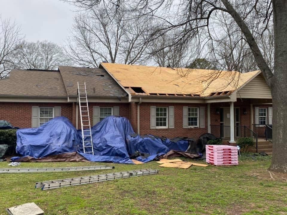 House with roofing construction: partially new roof, covered materials, ladder, brick siding, overcast sky.