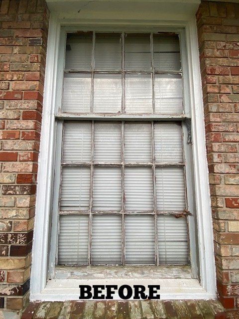 A deteriorated, white-framed window on a brick exterior before renovation. Blinds visible through the glass.