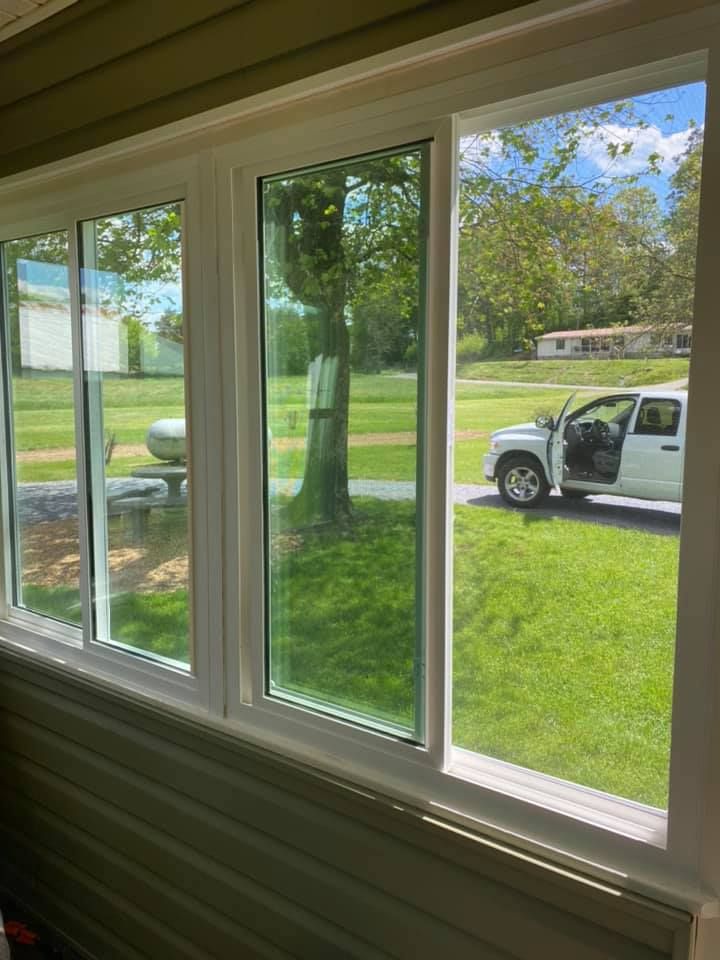White-framed windows overlooking a green lawn with a tree, a white truck, and a blue sky.
