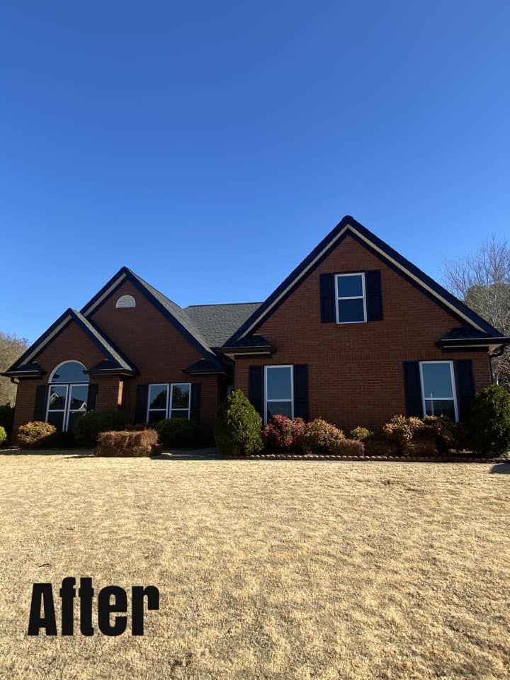 Brick house with dark roof and trim, blue shutters, and clear sky on a sunny day.