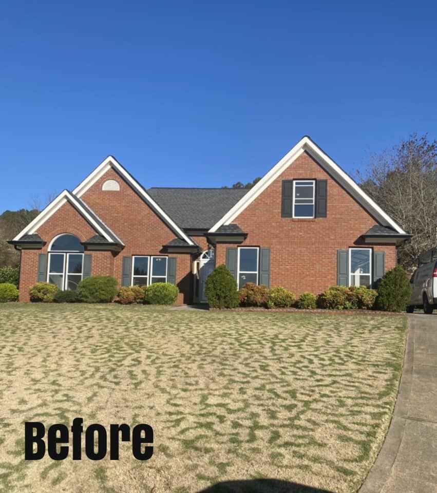Brick house with gray roof and shutters, front yard with sparse grass, sunny day.