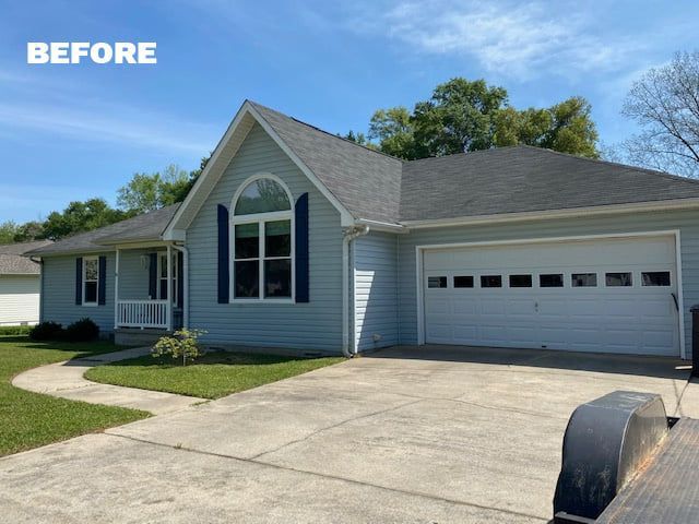 Light blue house with grey roof, white garage door, and a concrete driveway under a blue sky.