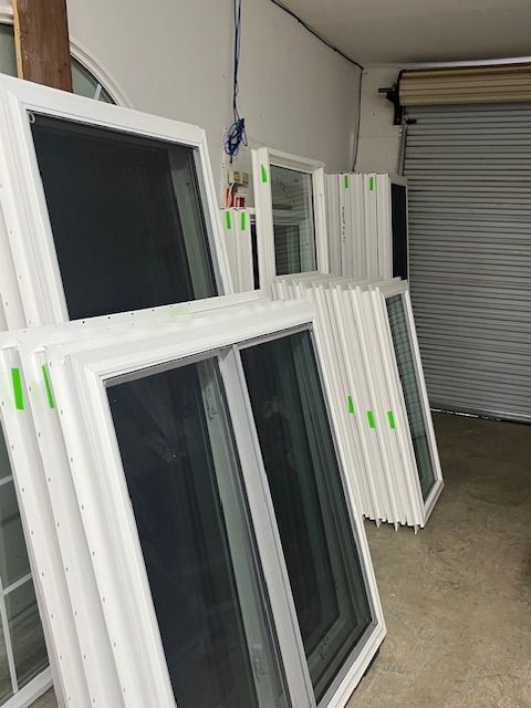 White window frames stacked against a wall with a gray garage door in the background.