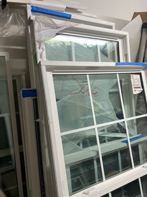White framed windows stacked together, protected with wrapping and blue tape.