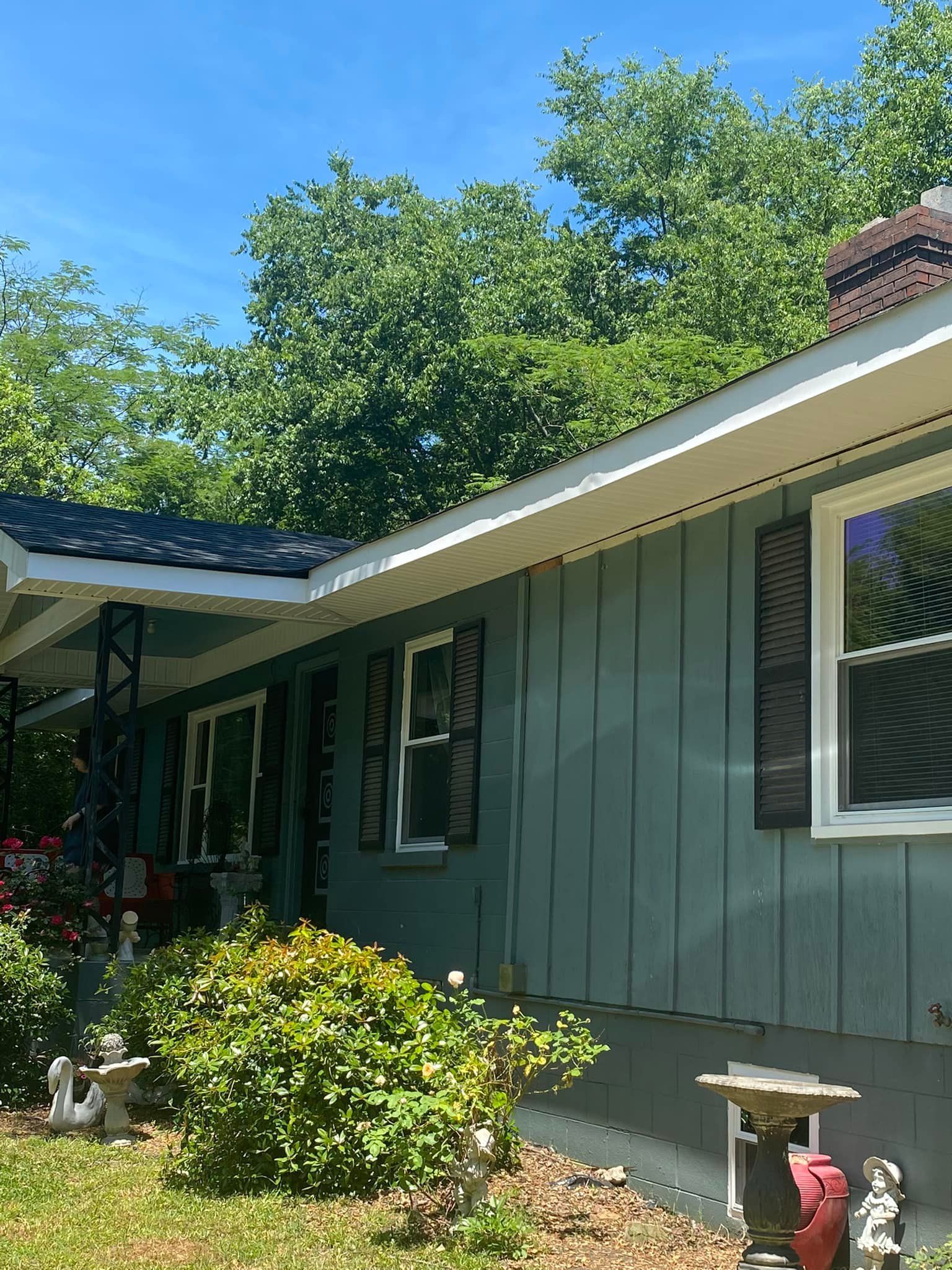 Blue house with white trim, brown shutters, and chimney. Overgrown bushes in front.