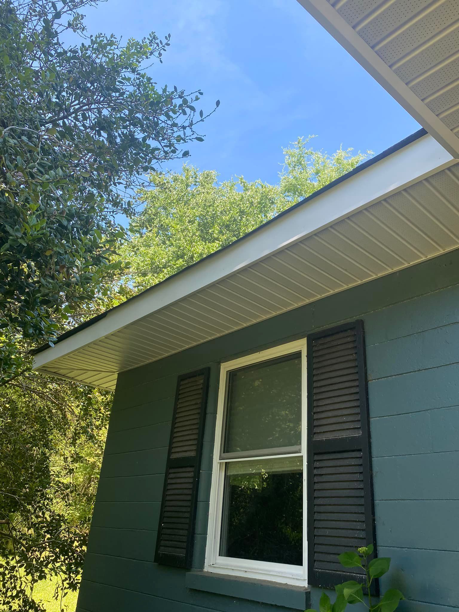 Exterior of a house with teal siding, a window with black shutters, and white trim under a light blue sky.