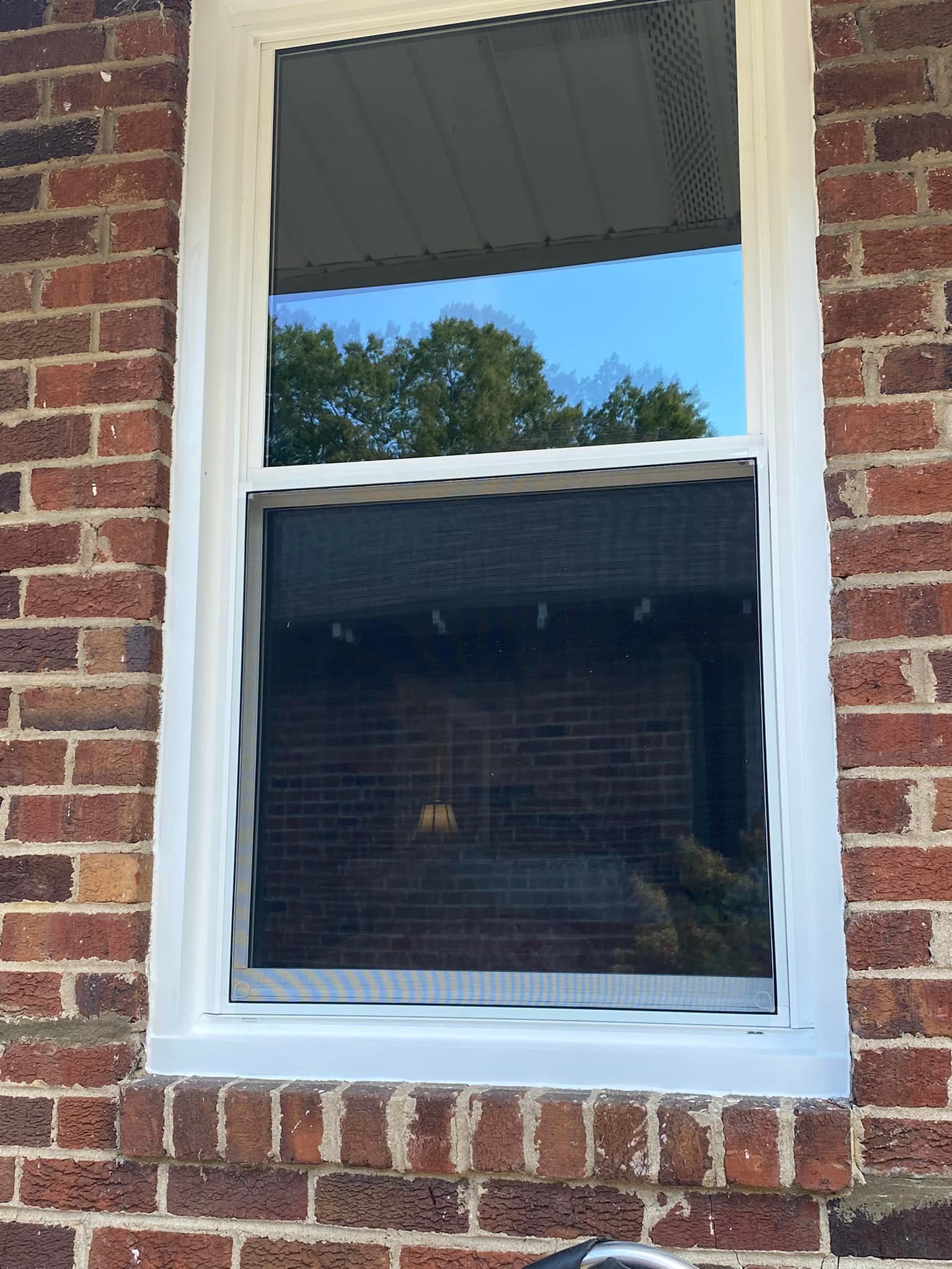 White-framed window in brick building; the window's upper half is clear, the lower half has a screen.