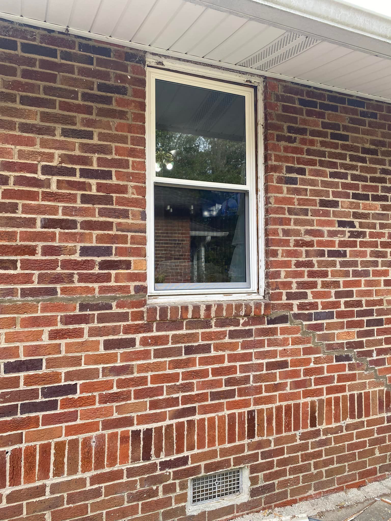 Brick exterior wall with a window; white trim, vent below.