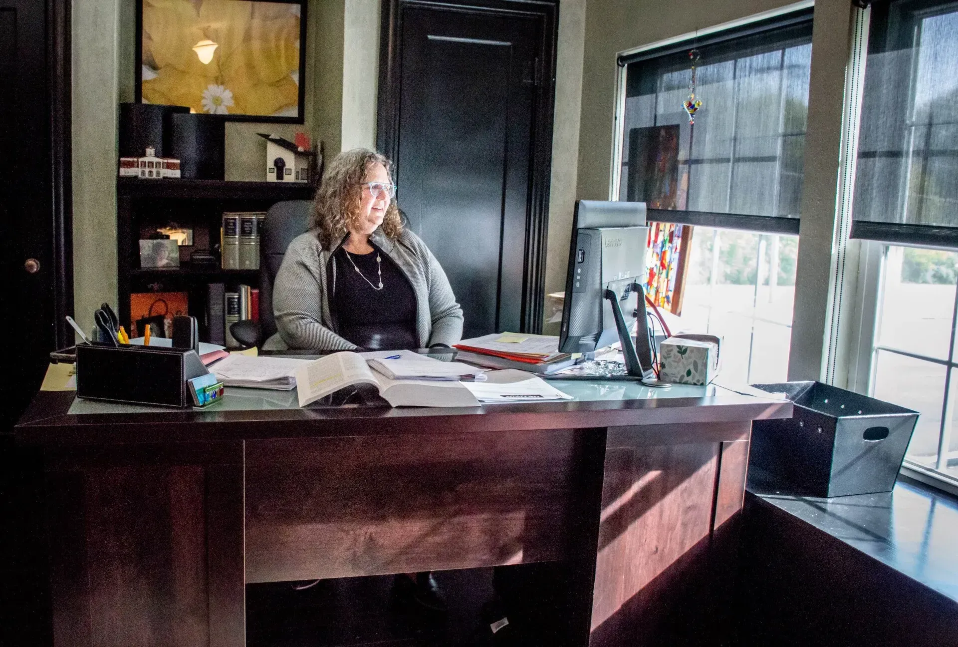 Woman at desk in office, looking at computer screen. Books and papers are present.