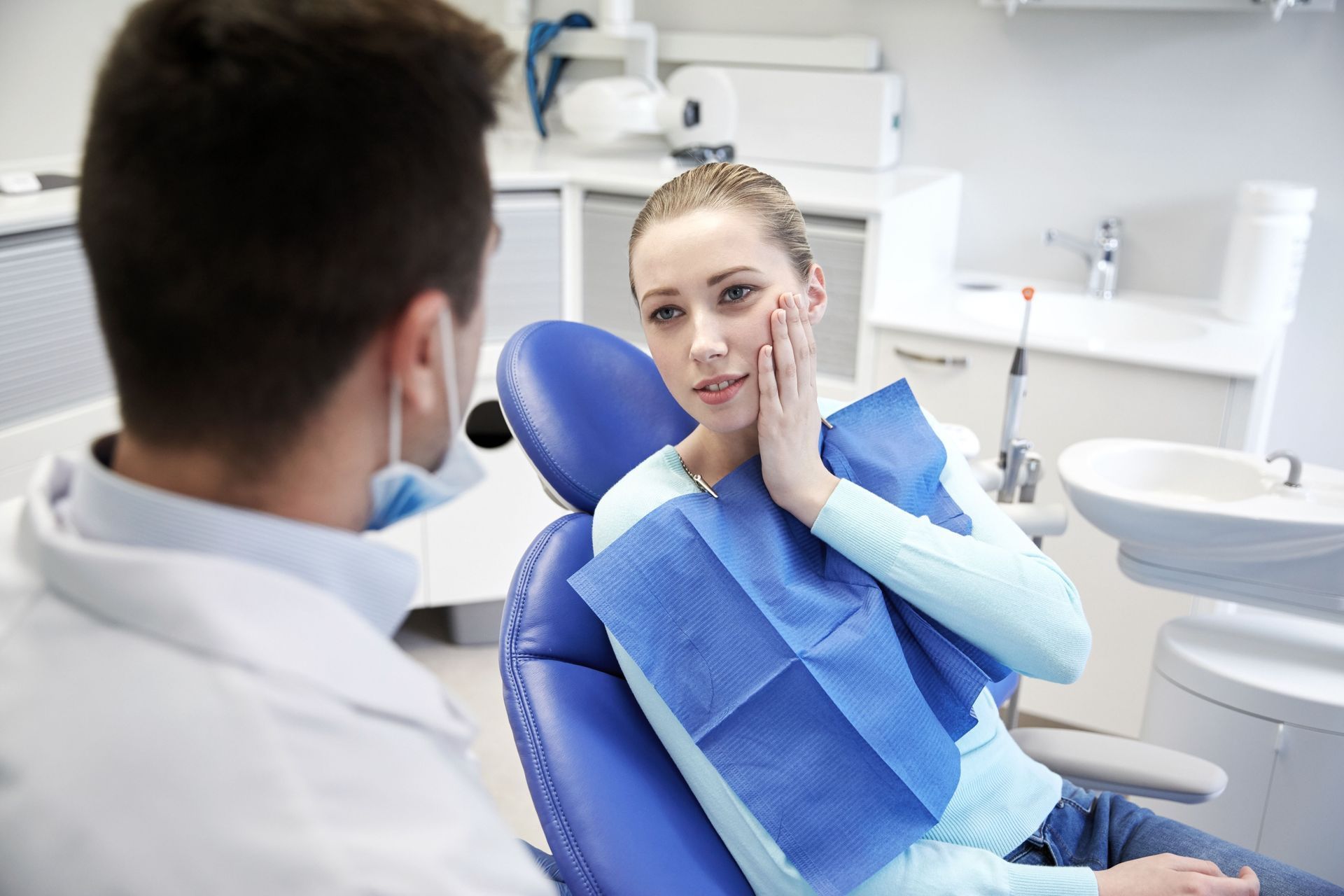 Patient in blue dental bib chatting with a dentist in a bright exam room