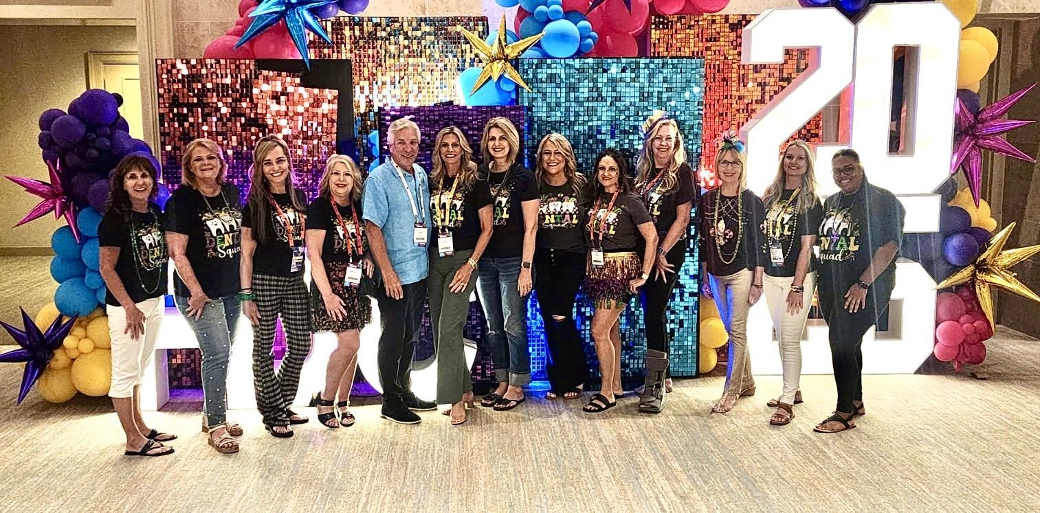 Group of people posing in front of a colorful balloon wall and large “20” sign at a celebration event