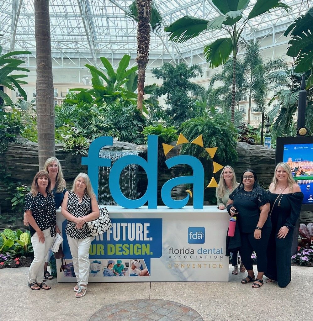 Group posing by a large “fda” sign in a bright indoor garden atrium, with a “Future is our design” display.