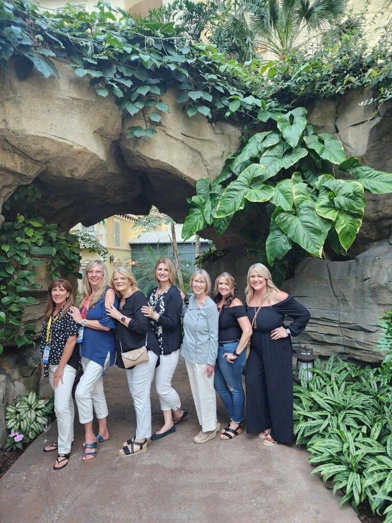 Six people posing in a lush stone archway garden, smiling for a group photo