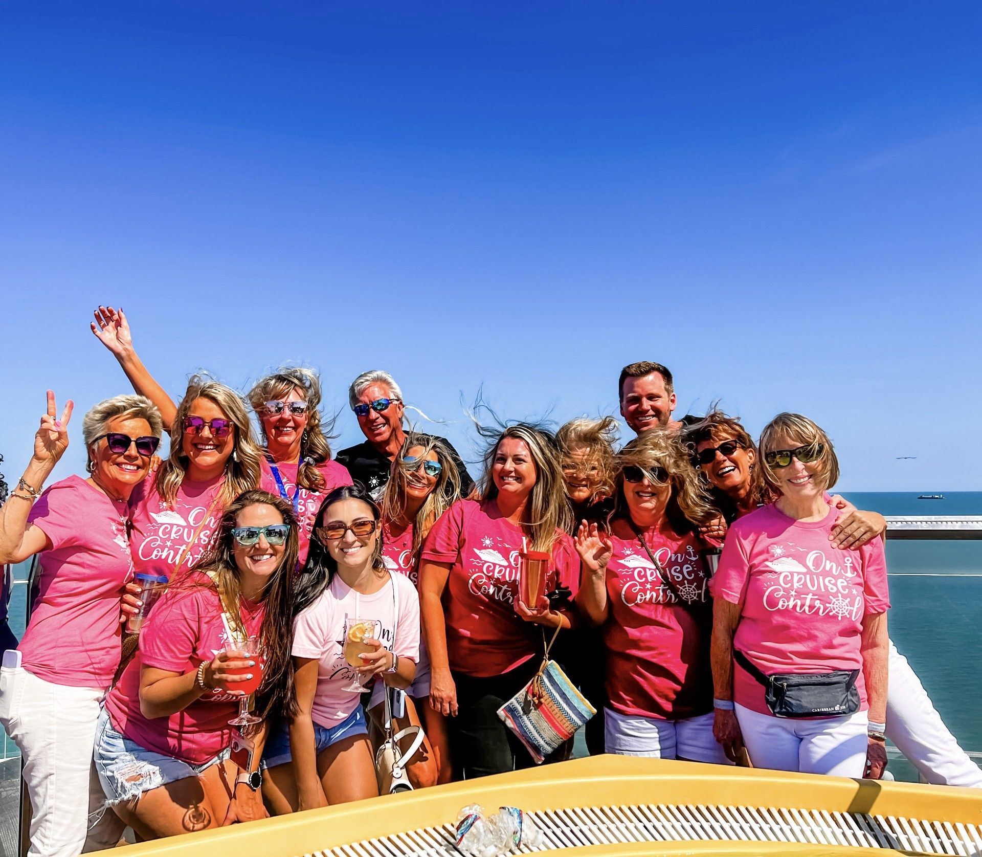 Group of smiling people in pink shirts posing on a sunny boat deck under a clear blue sky