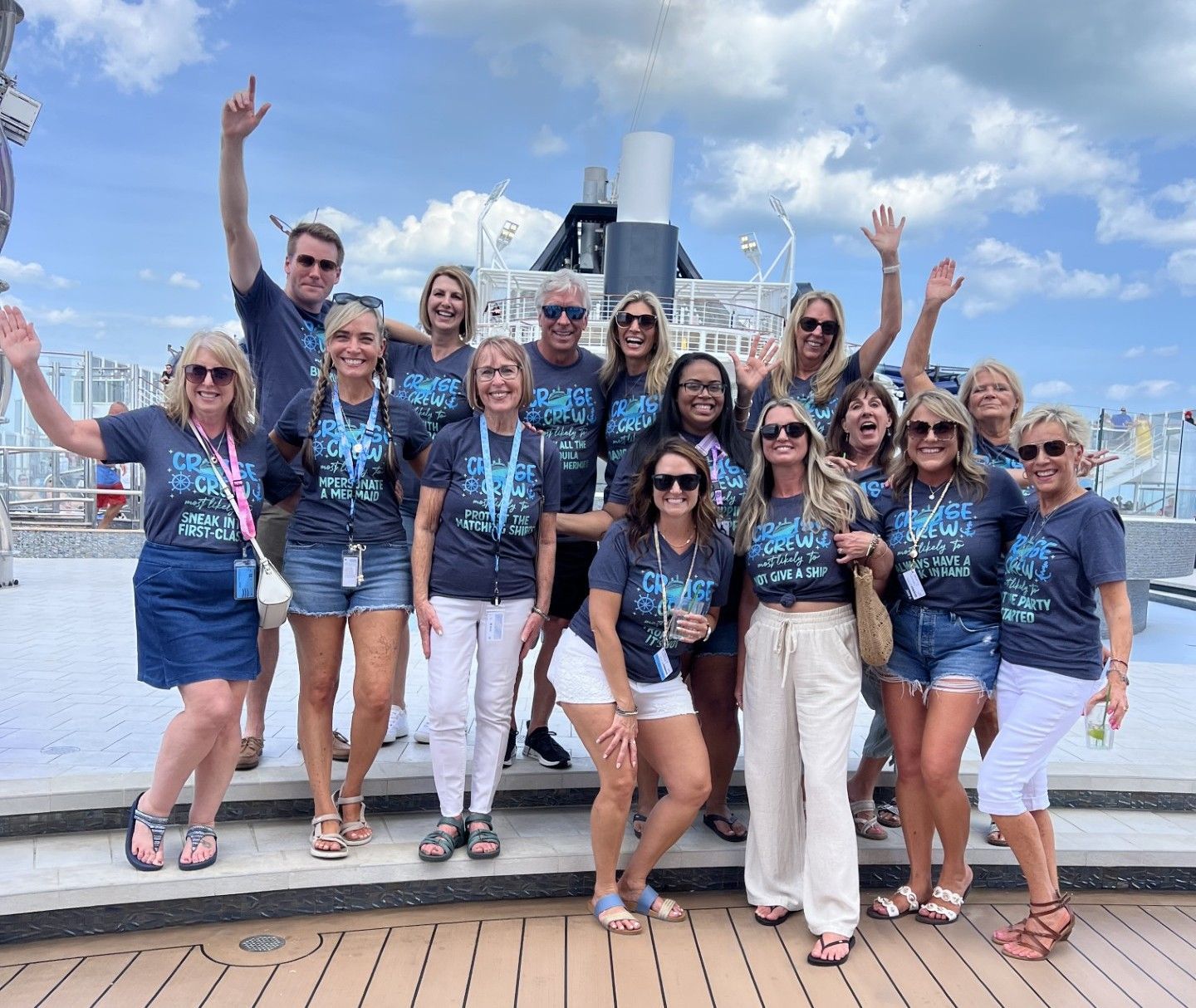 Group posing outdoors on a ship deck, smiling and waving with a city skyline in the background.