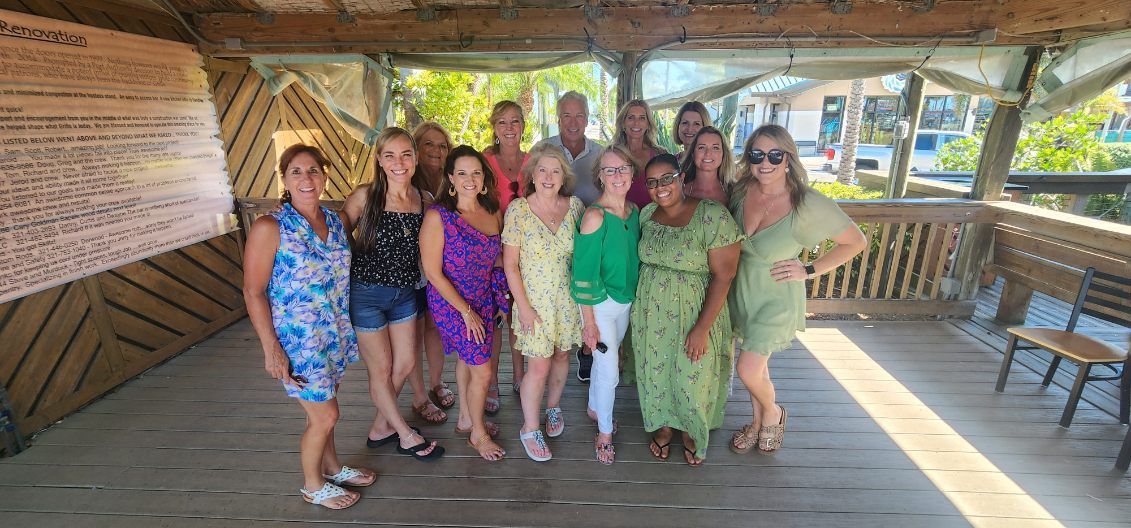 Group of women in colorful dresses posing together on a wooden pavilion by the water