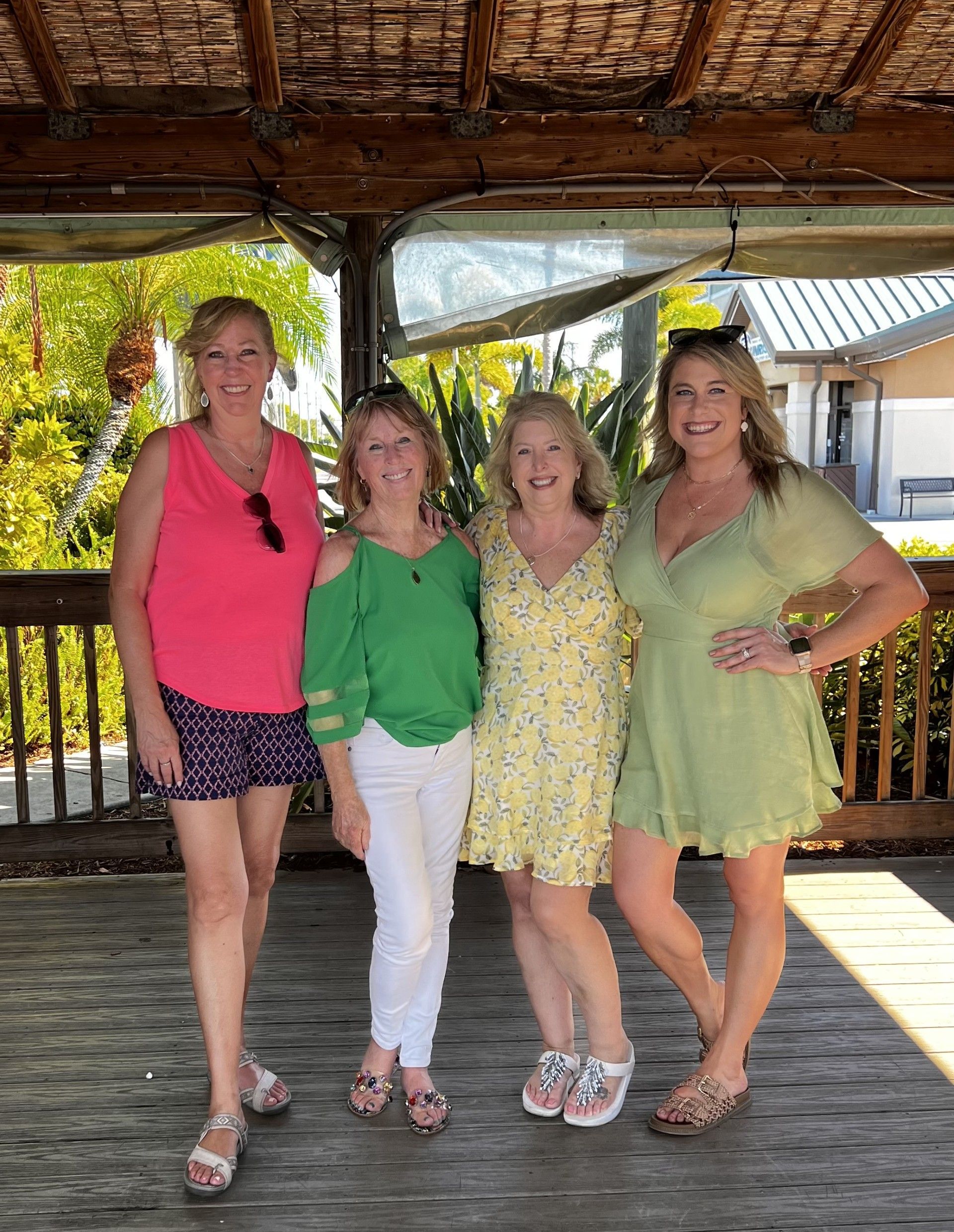 Four women posing together under a wooden pavilion, smiling in colorful summer outfits.