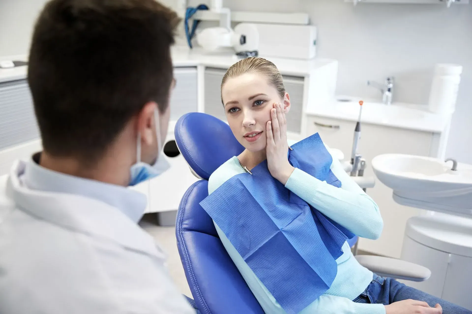 Patient at dentist’s office receiving a dental exam, with blue bib and chair in a bright clinic.