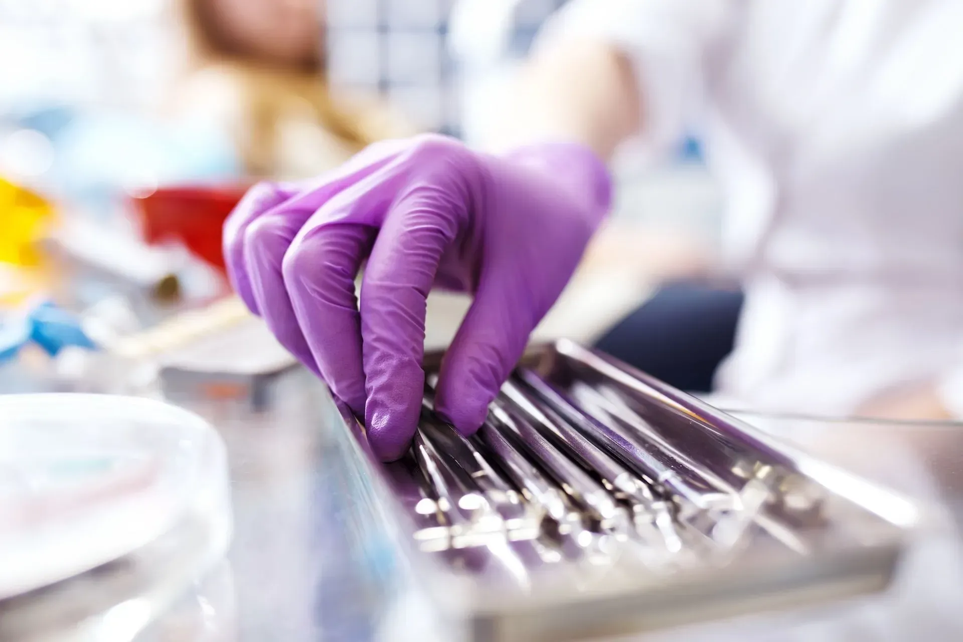 Purple-gloved hand arranging metal tools on a tray in a clinical setting