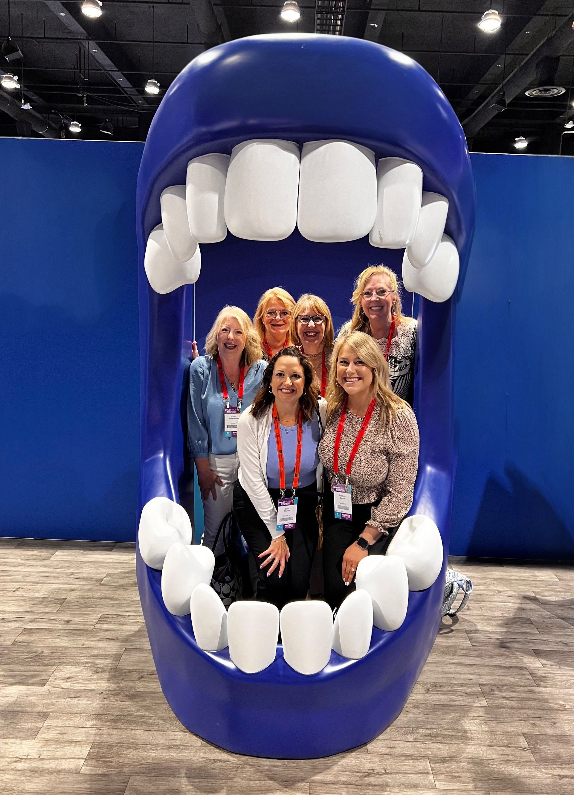 People posing inside a giant blue mouth with white teeth at an indoor event