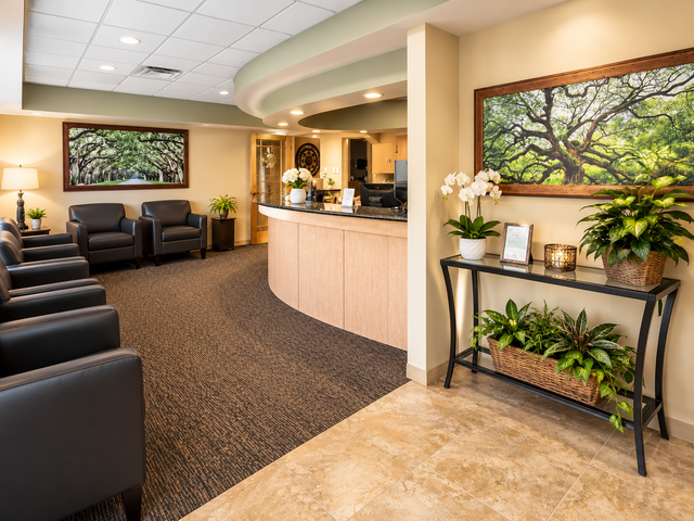 Modern office waiting area with black chairs, reception desk, patterned carpet, and potted plants