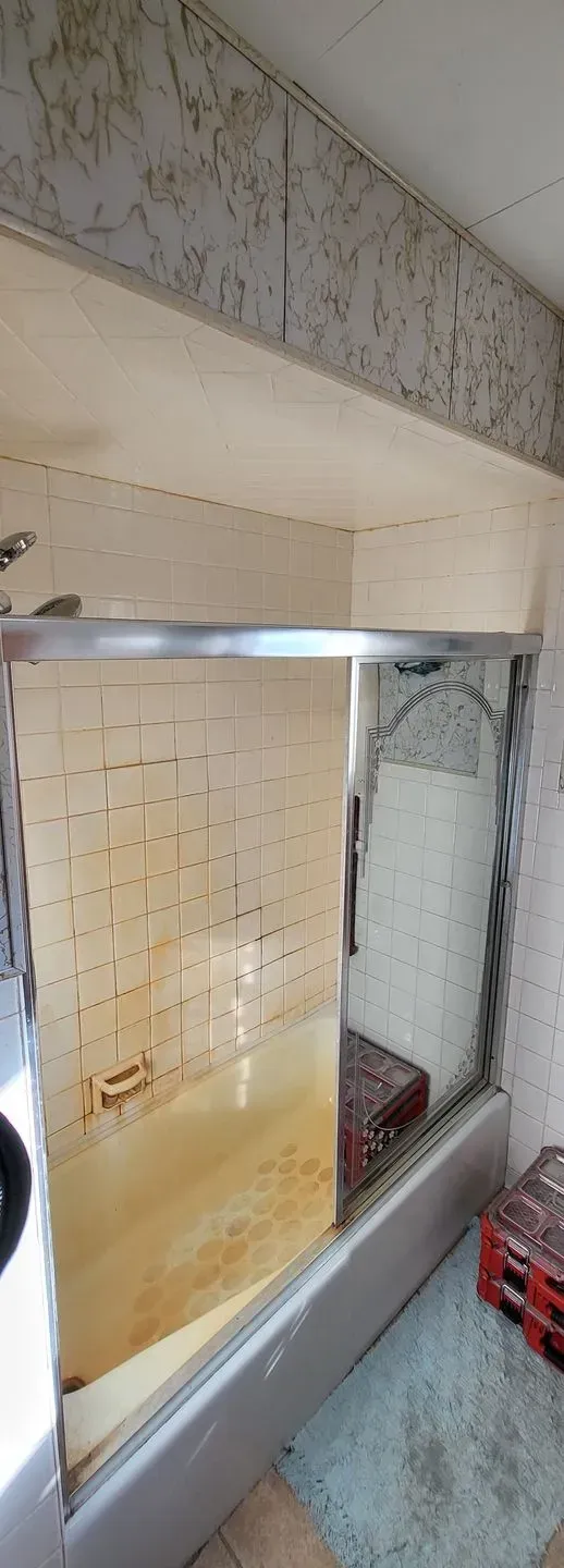 A dirty, stained shower with a glass door, possibly mold. Pallet in the shower.