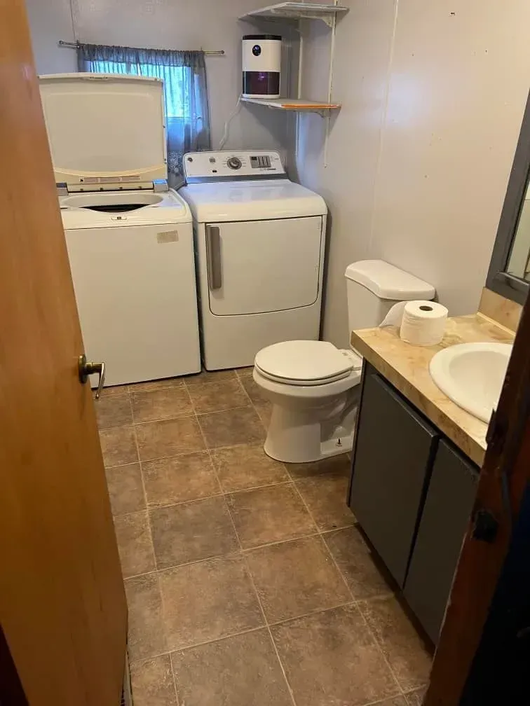 Laundry room with a washer, dryer, toilet, and sink. Brown tile floor and light blue walls.