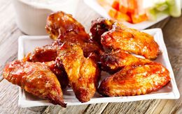 Plate of glazed chicken wings with vegetable sticks on the side