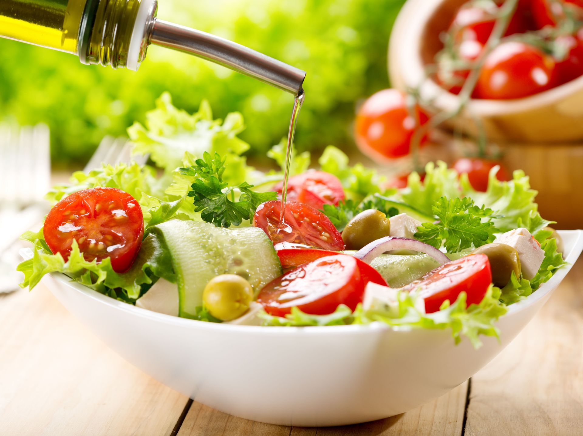 Fresh salad with tomatoes, cucumber, lettuce, and olives in a white bowl on a wooden table