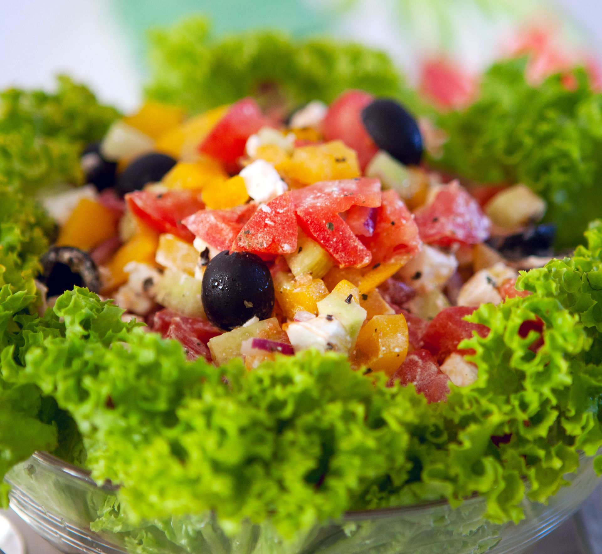 Fresh vegetable salad with lettuce, tomatoes, olives, and diced peppers in a glass bowl