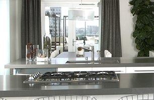 Modern kitchen with a stainless steel island, stove, pendant lights, and large window views.