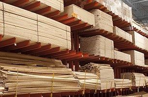 Stacks of lumber and wooden boards stored on industrial warehouse racks.